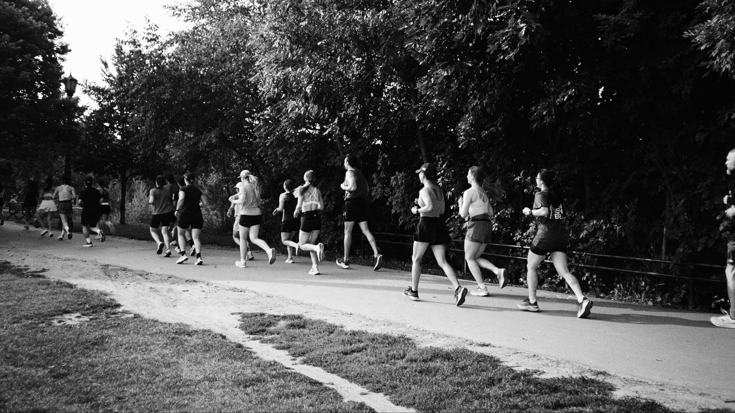 Black and white photo of a group of people running on a path with trees in the background